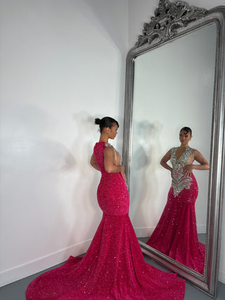 A glamorous woman in a sparkling pink Alglist gown poses beside an ornate mirror, showcasing the gown's dramatic train and intricate embellishments