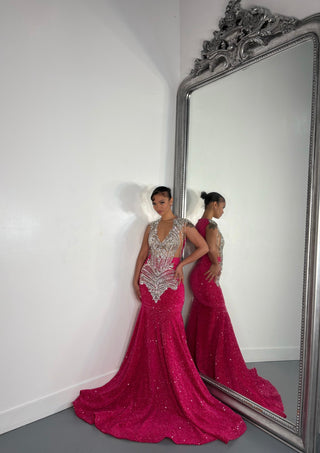 A person poses in a stunning pink Alglist gown adorned with sparkles and intricate beadwork, reflected in a vintage ornate mirror