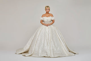 A model in an elegant off-the-shoulder wedding gown from Aglist with intricate lace details and a sweeping train, against a neutral background