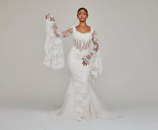A woman in an elegant white lace wedding dress from Alglist with long, flowing sleeves and intricate floral patterns, standing confidently against a neutral backdrop