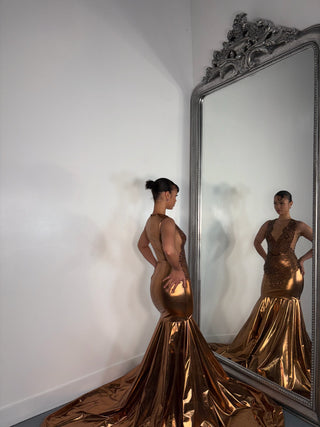 A woman models a stunning, metallic bronze gown with a flowing train, reflected in an ornate, vintage-style mirror